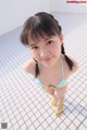 A little girl in a bikini standing on a tiled floor.