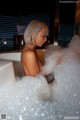 A woman sitting in a bathtub filled with foam.