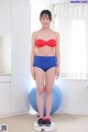 A woman in a red bra top and blue shorts standing on a scale.