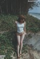 A woman in a white tank top standing on a rock by the ocean.