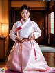 A woman in a pink and white hanbok is posing for a picture.